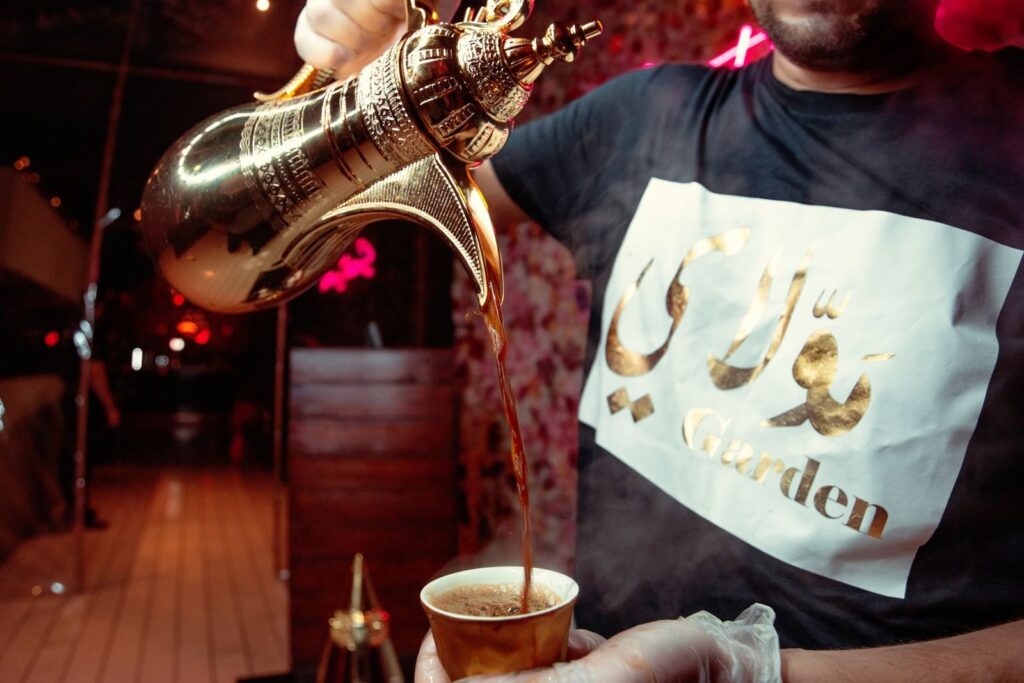 Arabian coffee being poured from a brass dallah into a small paper cup