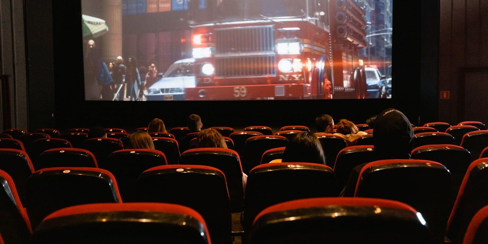 Audience in red cinema seats watching a fire truck scene on a large screen