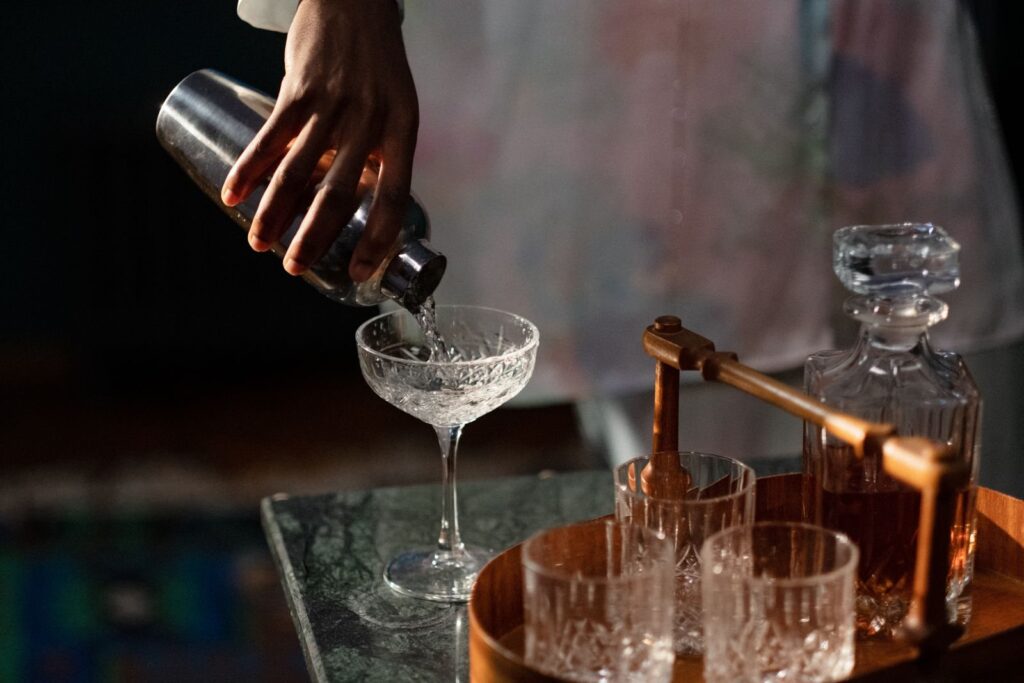 Bartender pouring a cocktail from a shaker into a coupe glass on a dim bar top