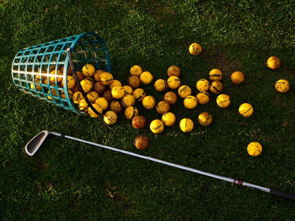 Basket of yellow range balls spilled on the grass beside an iron