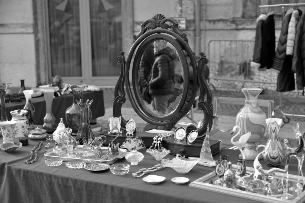 Black and white photo of an outdoor antiques table with a mirror, vases and silverware