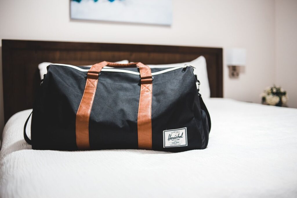 Black duffel bag on a white hotel bed