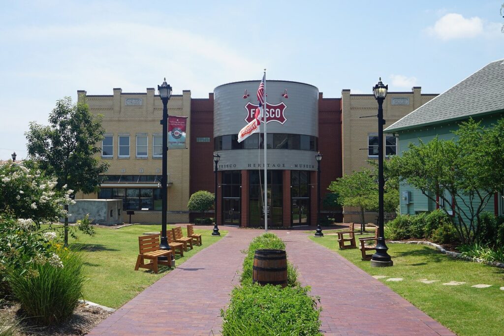 Brick walkway leading to the Frisco Heritage Museum with lampposts and a flagpole