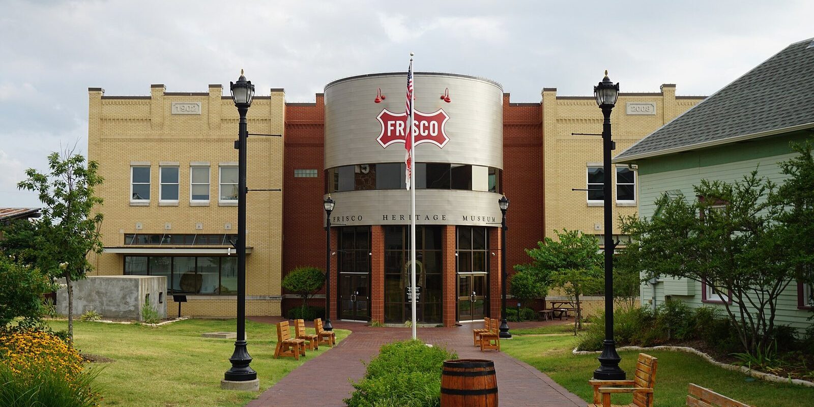 Brick walkway with benches and lampposts leading to the Frisco Heritage Museum entrance