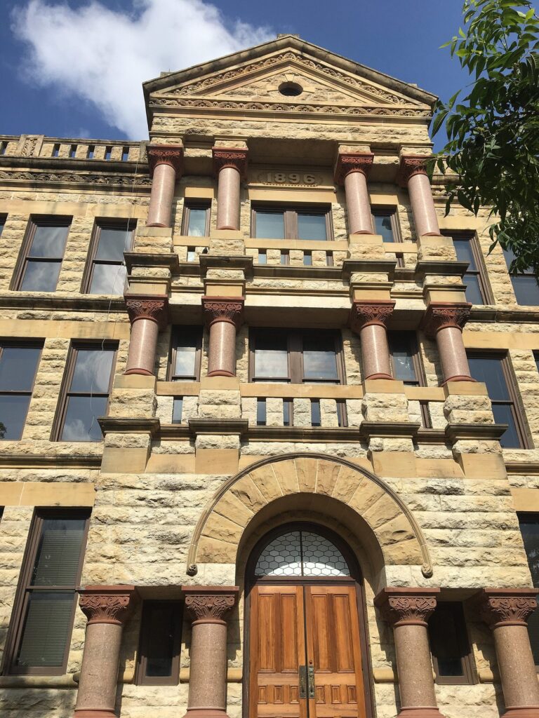 Carved limestone facade and red granite columns above the arched doors of the Denton County courthouse