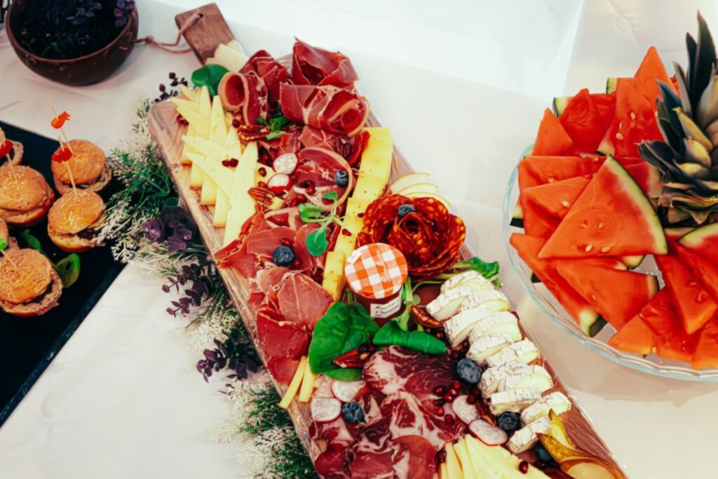 Charcuterie board with cured meats, cheese, fruit and small burgers on a party table
