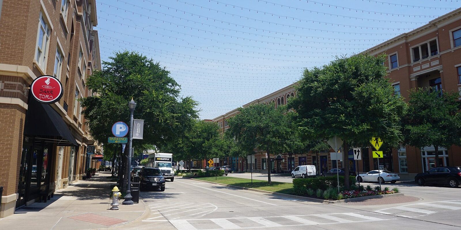 Coleman Boulevard near Frisco Square with brick buildings, shade trees and a parking sign