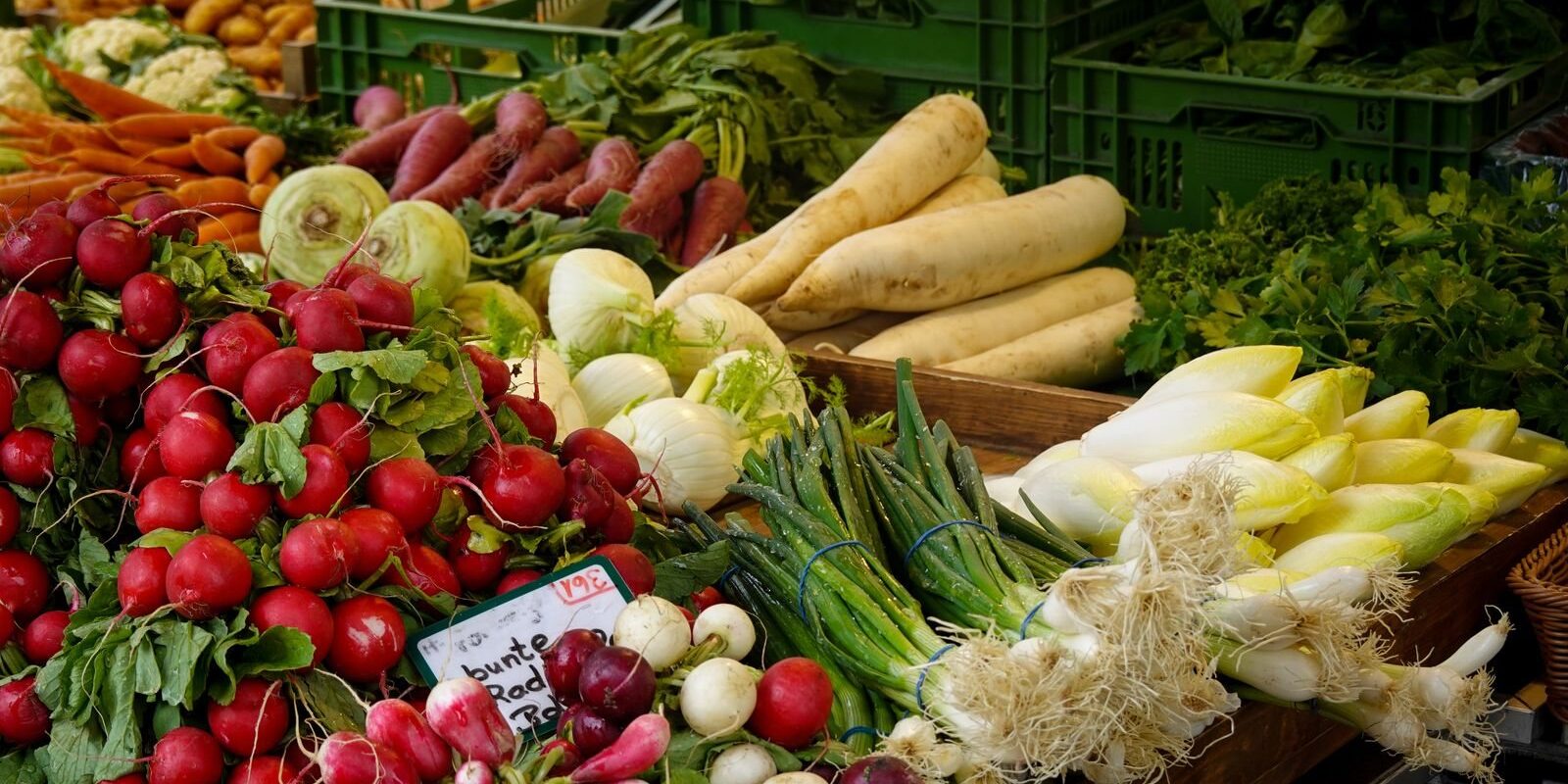 Crates of radishes, parsnips, leeks and spring onions on an outdoor produce stall