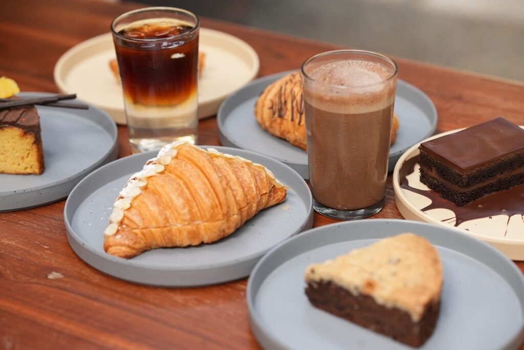 Croissant, iced coffee, hot chocolate and cake slices on grey plates