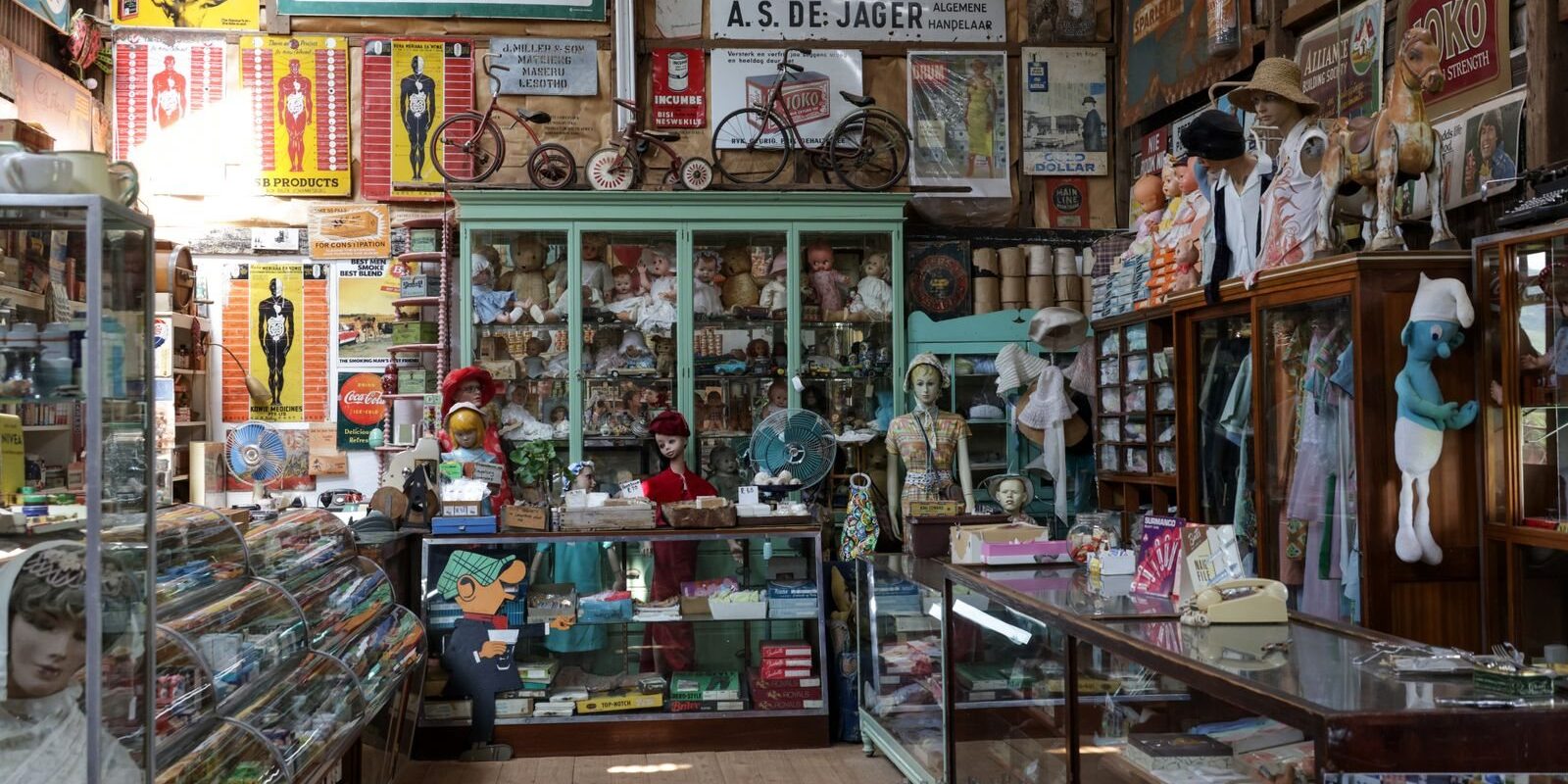 Crowded vintage shop with old signs, toys and glass cases, like the booths at antique shops in Frisco TX