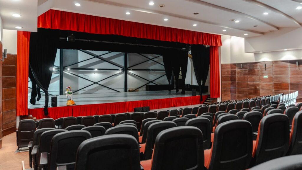 Empty theater with red curtains and rows of black seats facing a small stage