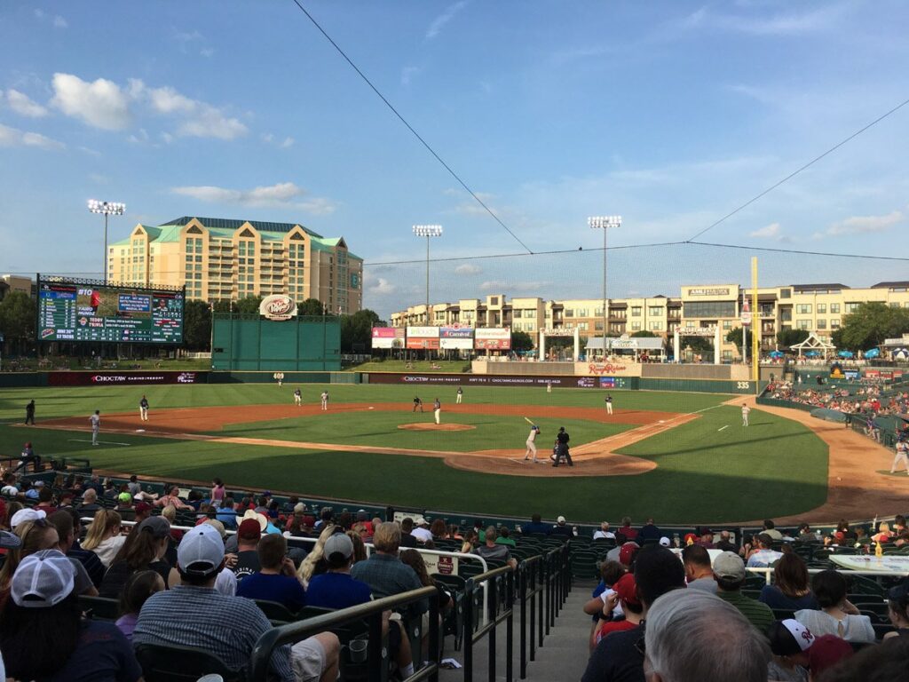 Fans in the stands watching a Frisco RoughRiders baseball game on a sunny evening