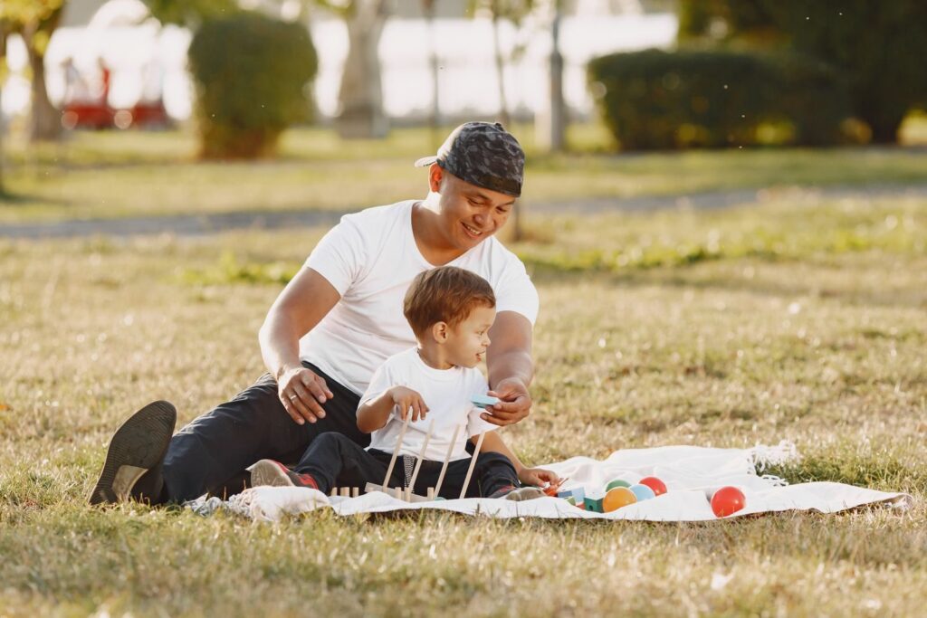 Father and toddler son playing together on a picnic blanket in a sunny park