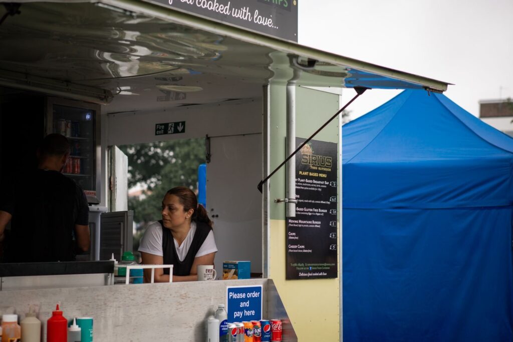 Food truck crew serving from a window at an outdoor festival with a blue canopy