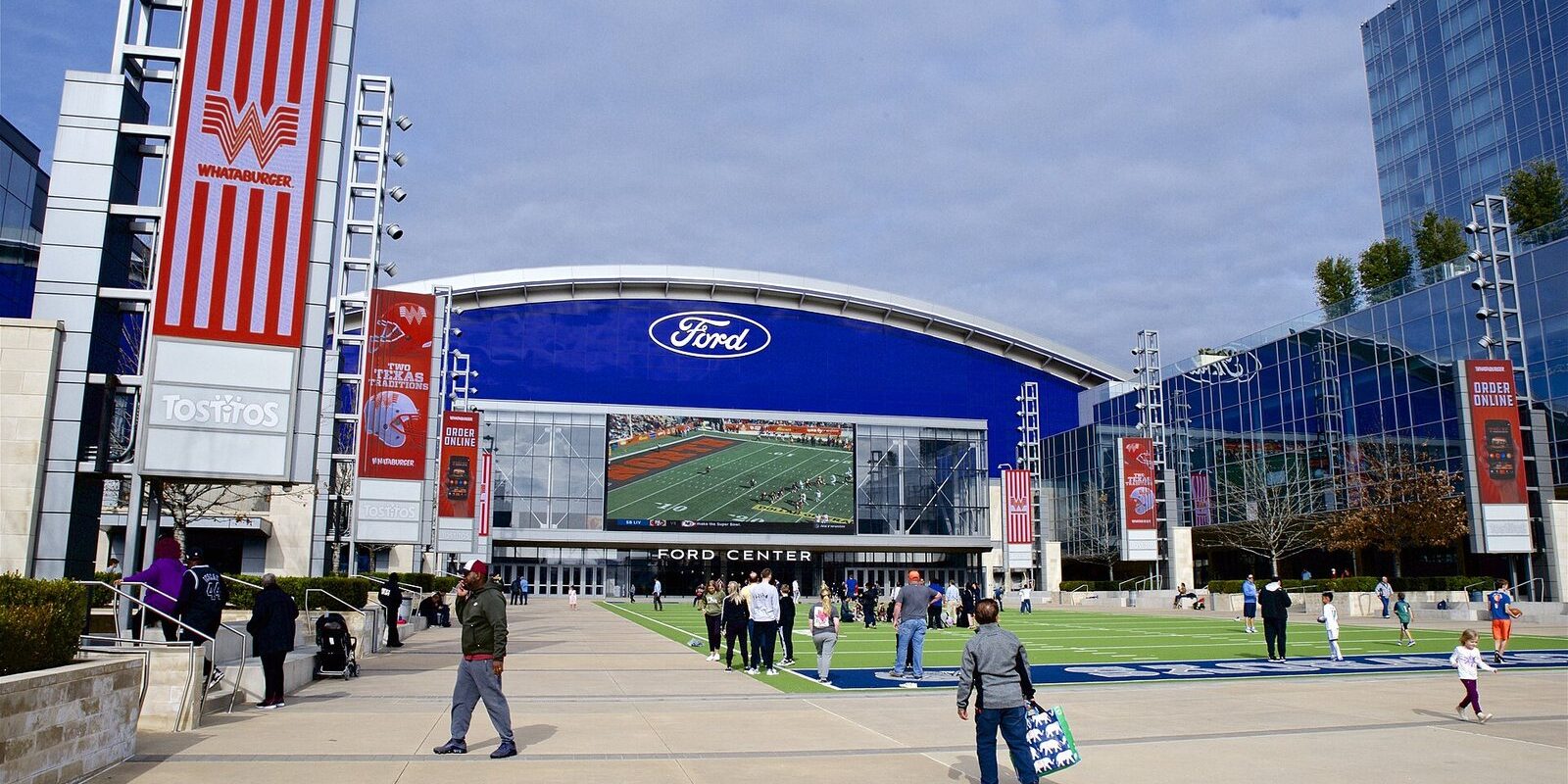 Ford Center at The Star with a giant video board above a turf plaza and people walking