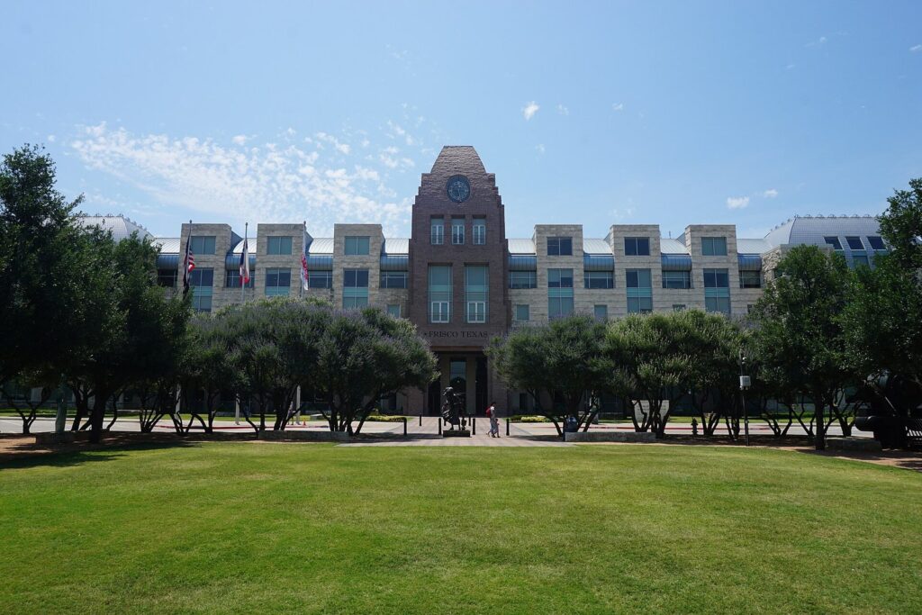 Frisco City Hall, a brick municipal building with a central tower, behind a wide lawn at Frisco Square