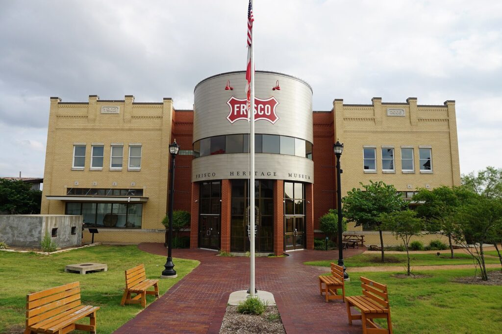 Frisco Heritage Museum building with a flagpole, brick walkway and wooden benches