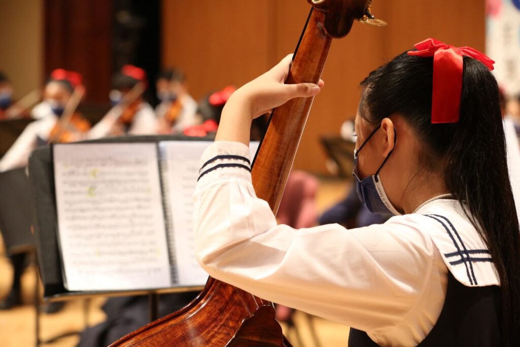 Girl in a white blouse playing double bass beside sheet music in an orchestra