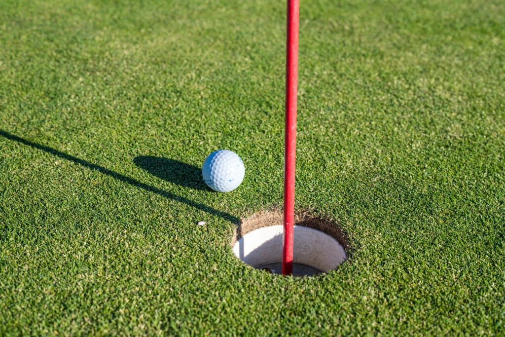 Golf ball resting at the lip of a cup beside a red flagstick