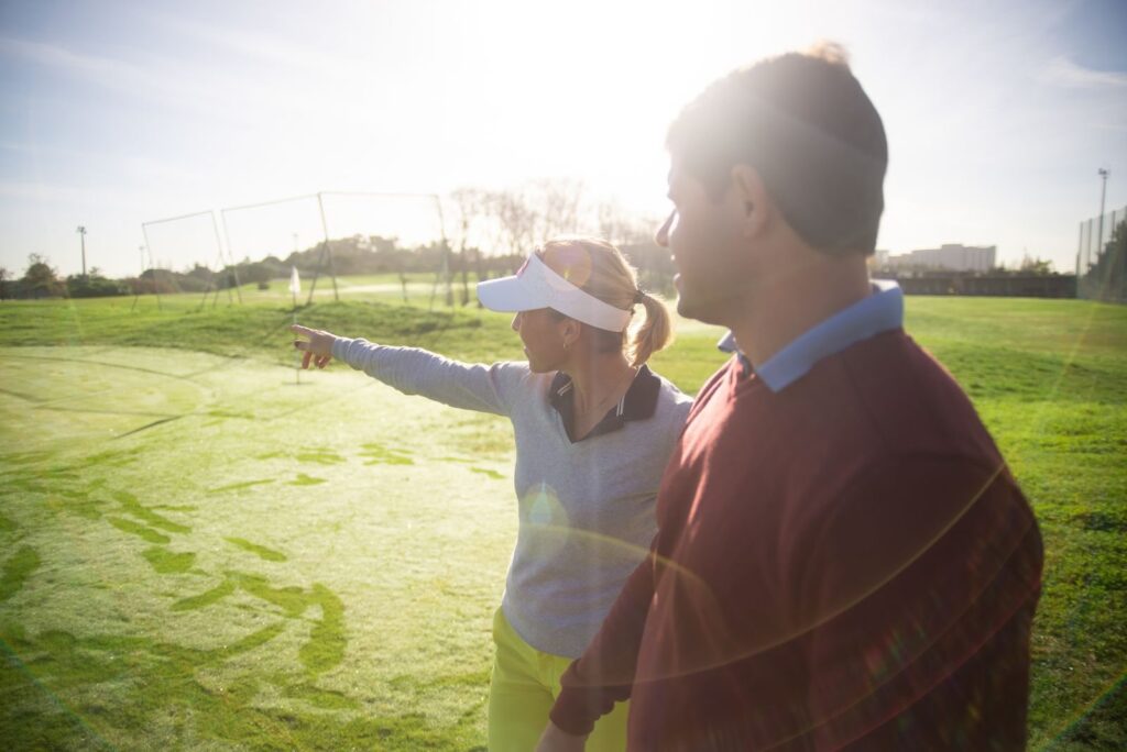 Golf coach in a visor pointing down the fairway while talking with a student