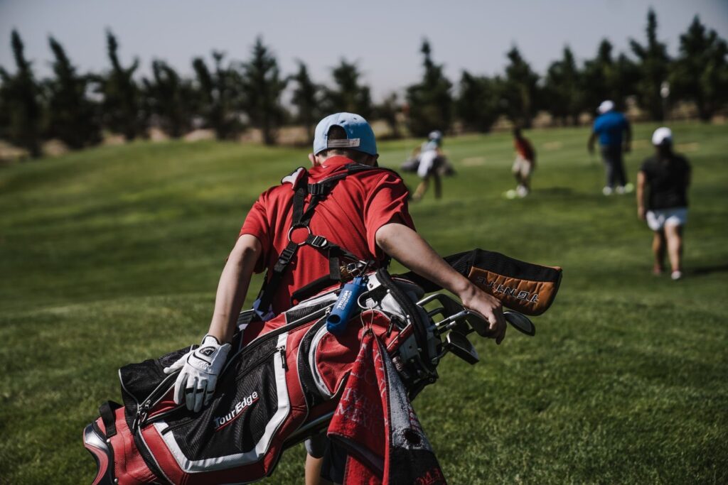 Golfer carrying a red stand bag across a fairway toward his playing partners