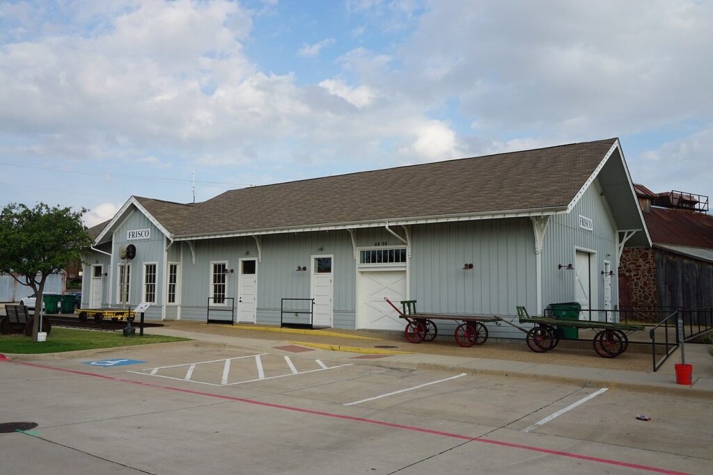 Gray railroad depot building with wagon carts at the Frisco Heritage Center