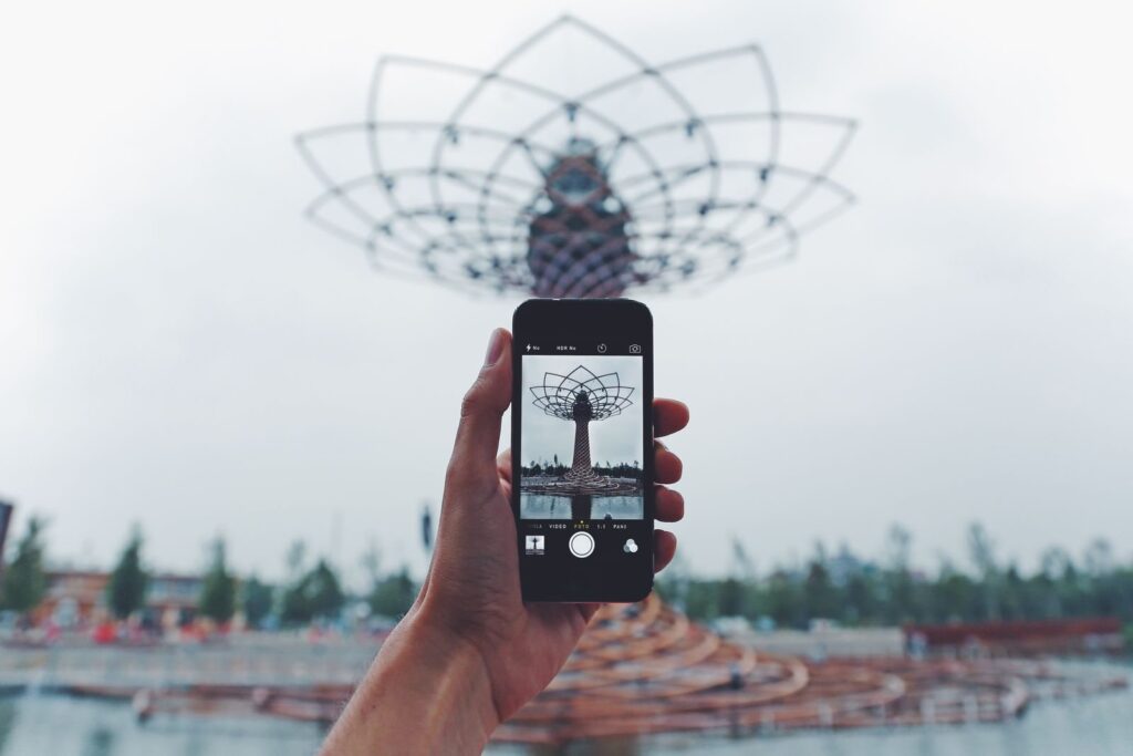 Hand holding a smartphone to photograph a large latticed metal structure