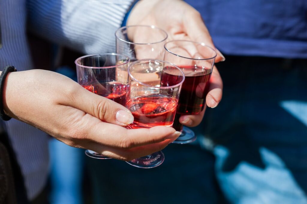 Hands holding small plastic cups of red wine at an outdoor tasting
