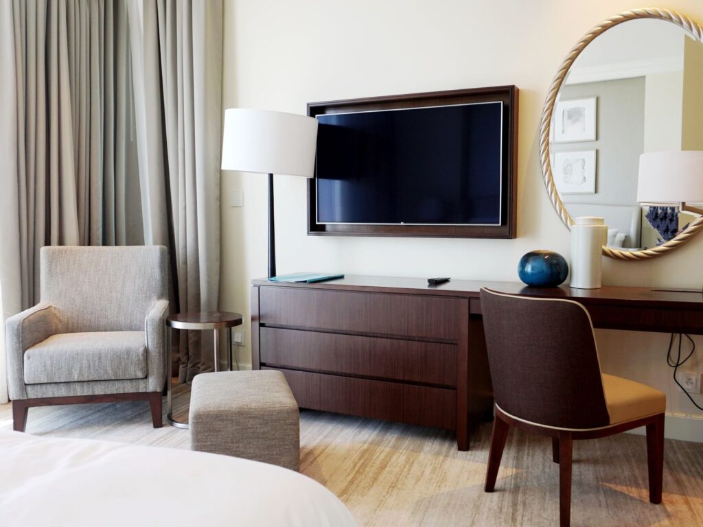 Modern hotel room with a desk, armchair and wall-mounted TV beside the bed
