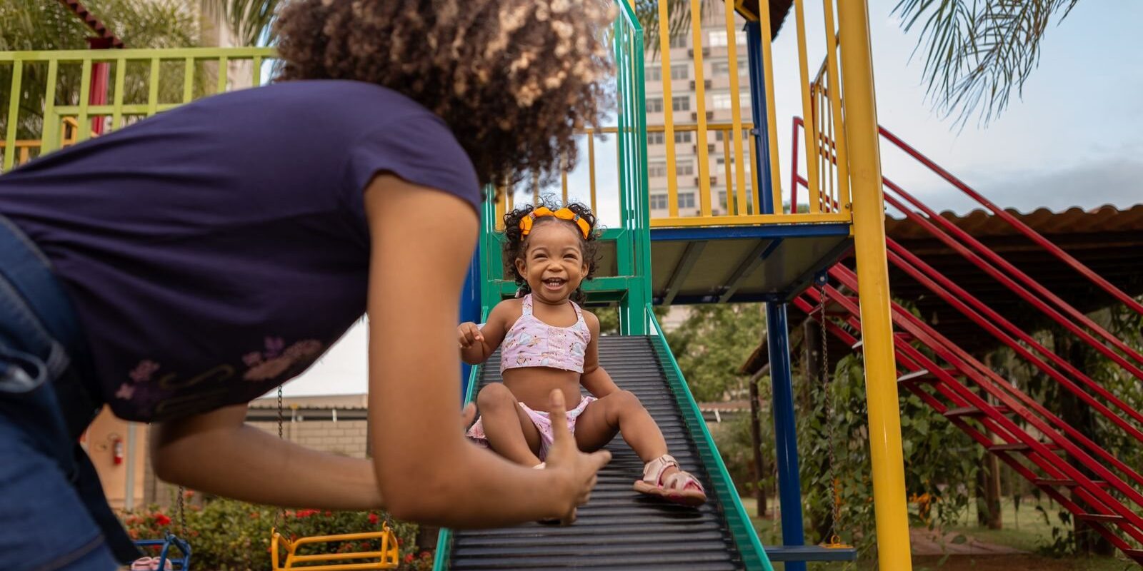 Mother catching her toddler daughter at the bottom of a playground slide on a sunny day