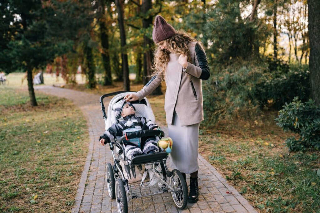 Mother in a long coat pushing a stroller along a brick path through an autumn park