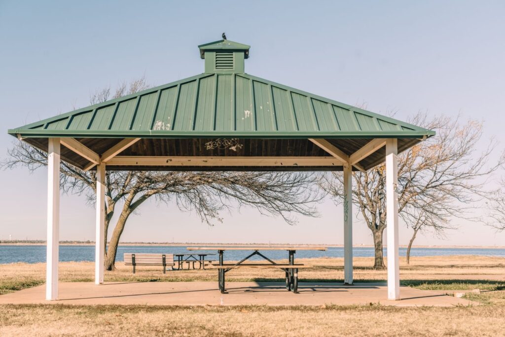 Open-sided pavilion with a green metal roof sheltering a picnic table