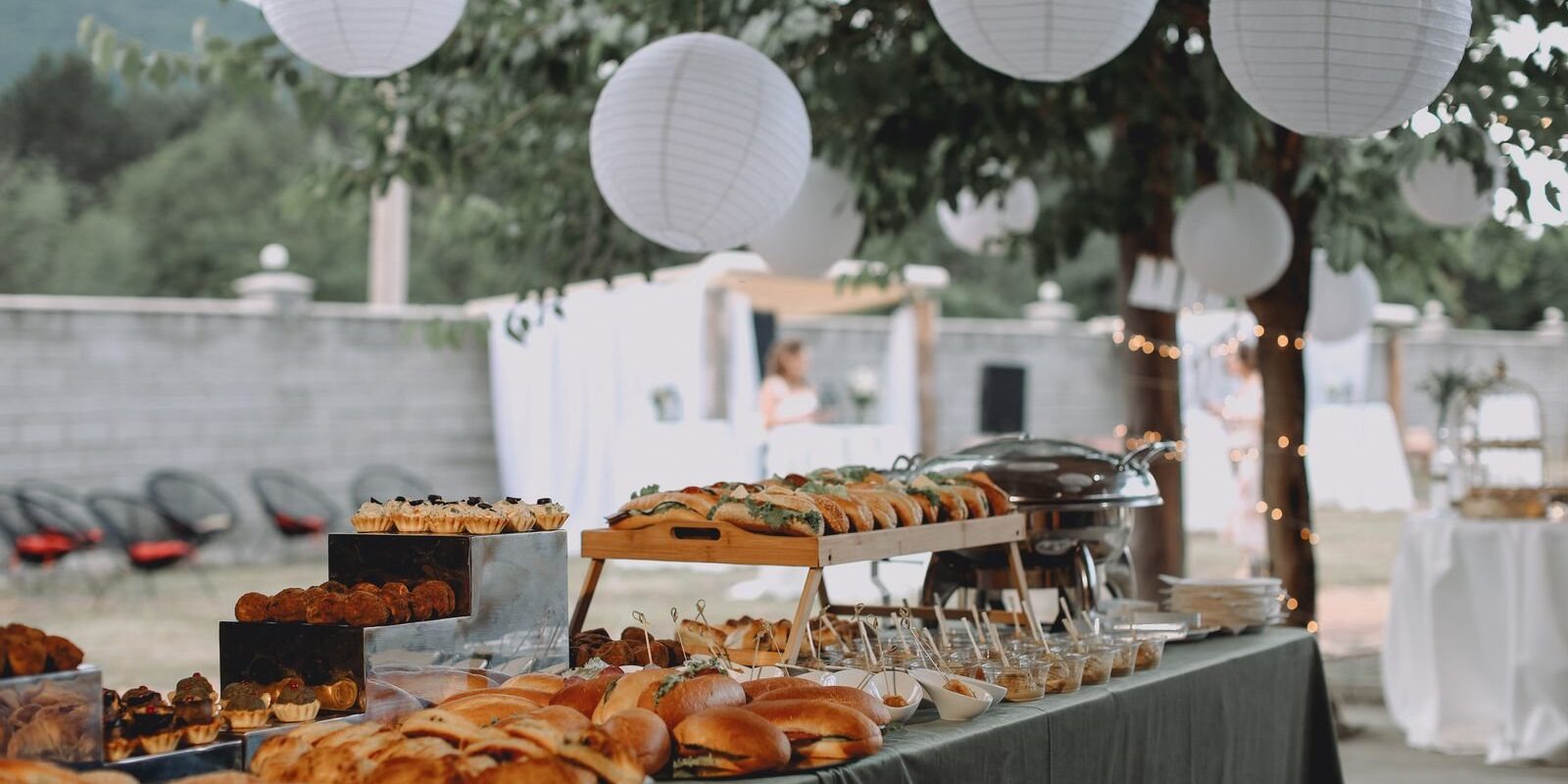 Outdoor buffet of sandwiches and pastries under paper lanterns, typical of catering in Frisco TX