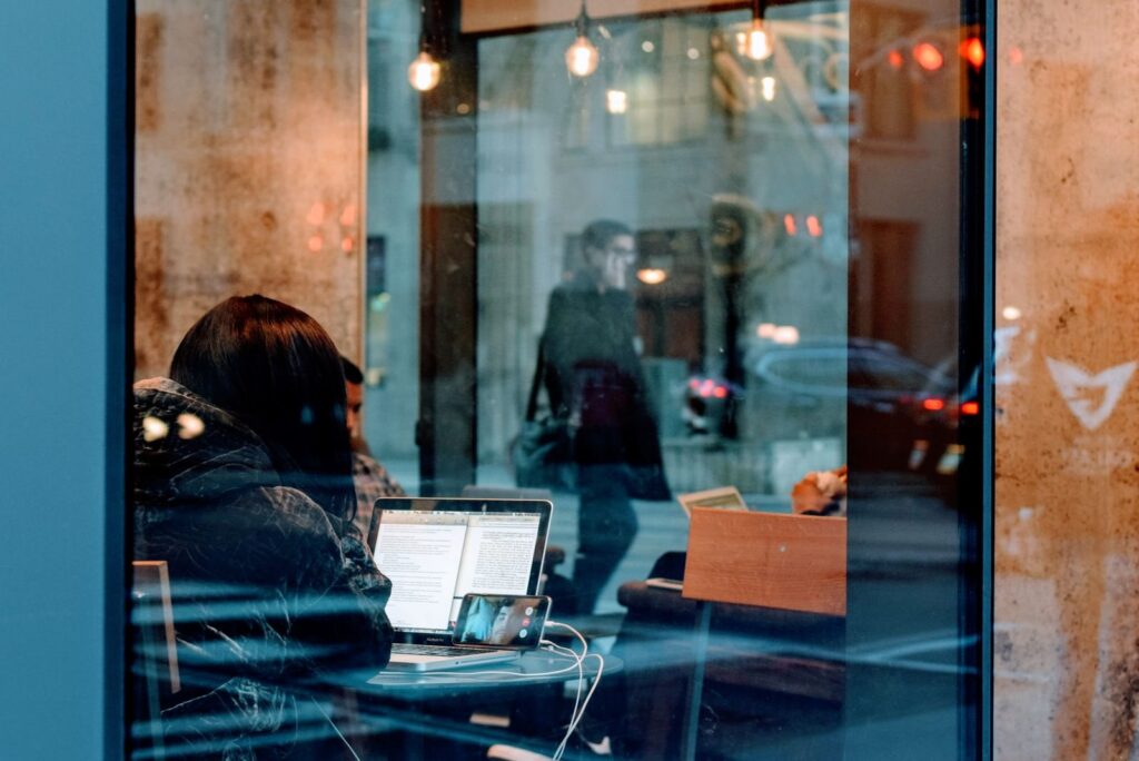 Person working on a laptop at a café table, seen through the front window