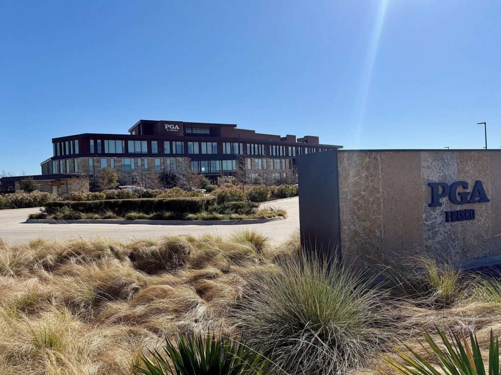 PGA of America headquarters building behind a stone PGA Frisco sign and native grasses