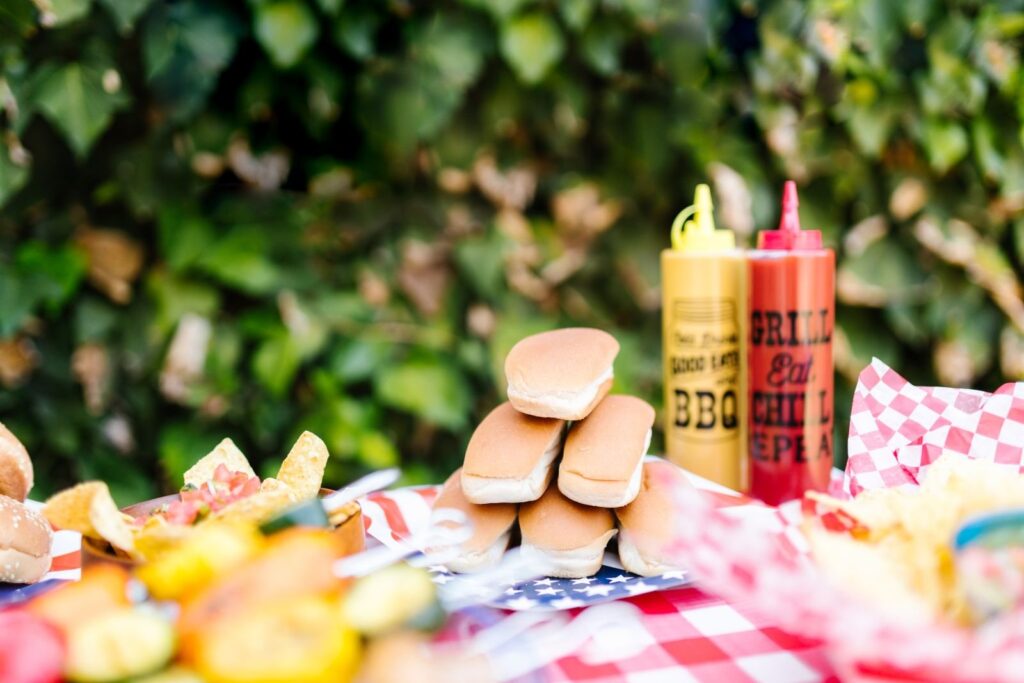 Picnic table with hot dog buns, barbecue sauce bottles and checkered paper