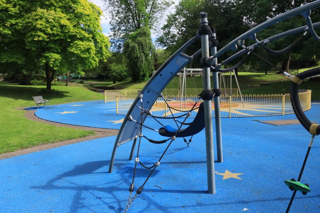 Playground with blue rubber surfacing and a curved metal climbing structure