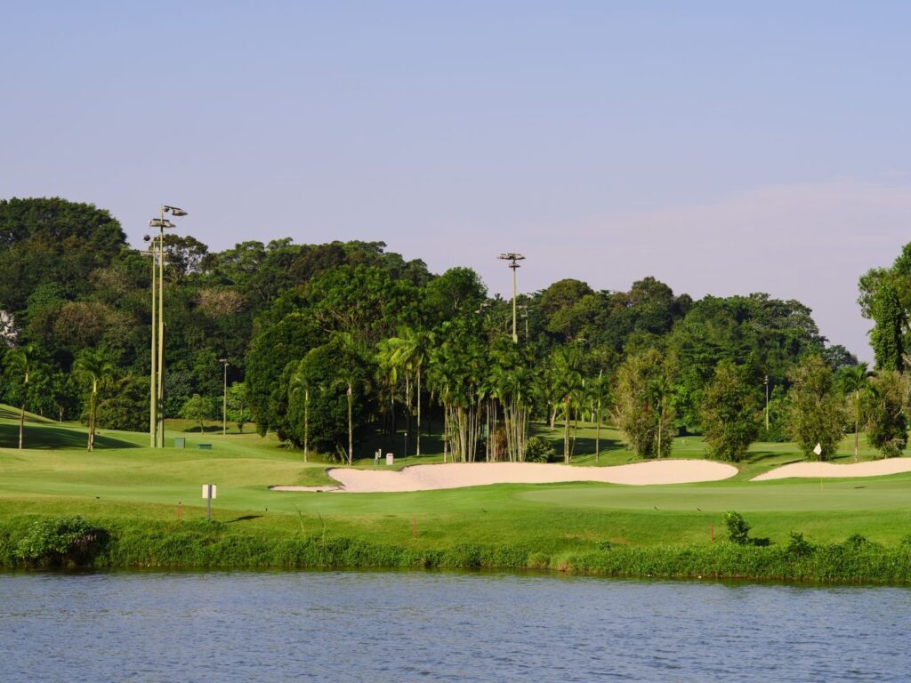 Pond in front of a green ringed by sand bunkers and tall trees