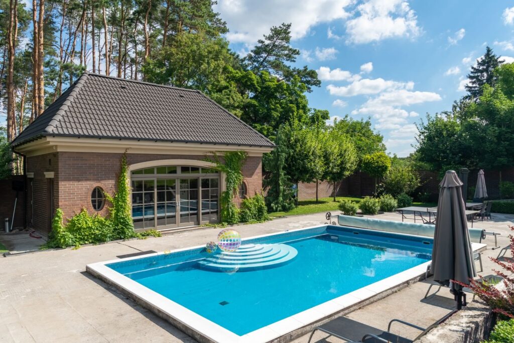 Private backyard swimming pool with lounge chairs beside a brick pool house on a sunny day