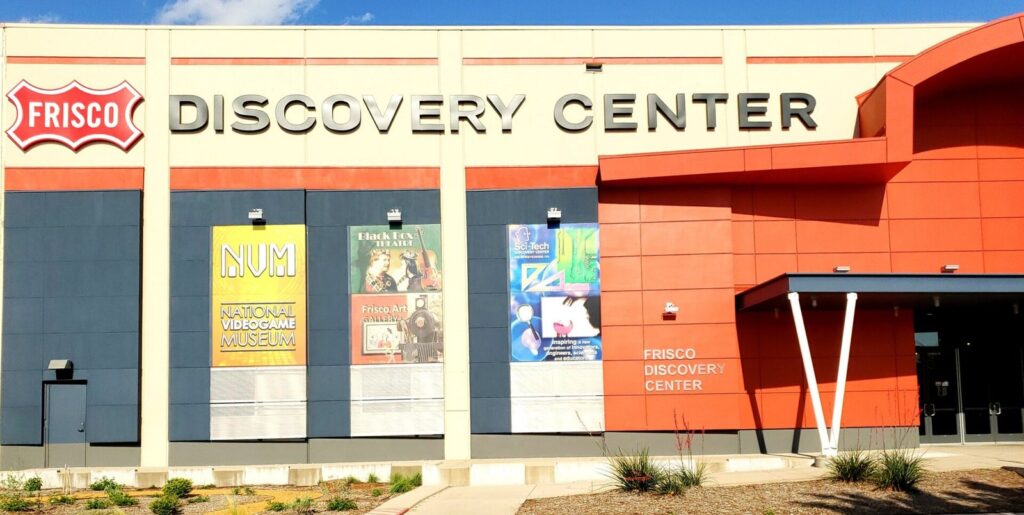 Red and cream facade of the Frisco Discovery Center with exhibit banners beside the entrance