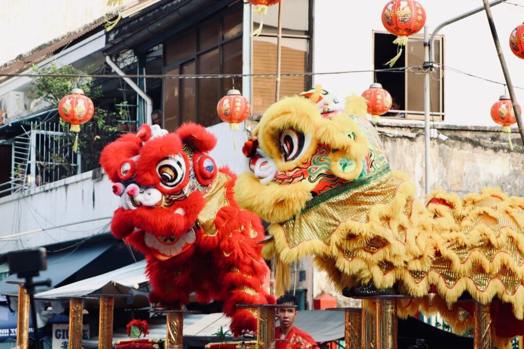 Red and yellow lion dance costumes performing beneath hanging paper lanterns