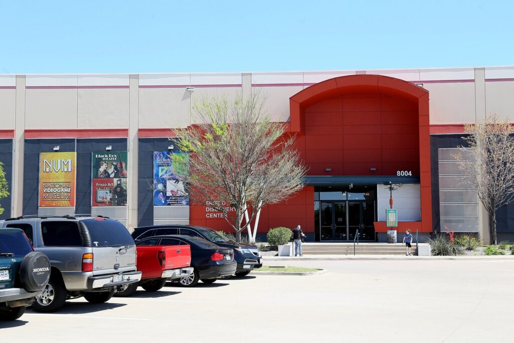 Red arched entrance of the Frisco Discovery Center with cars in the parking lot