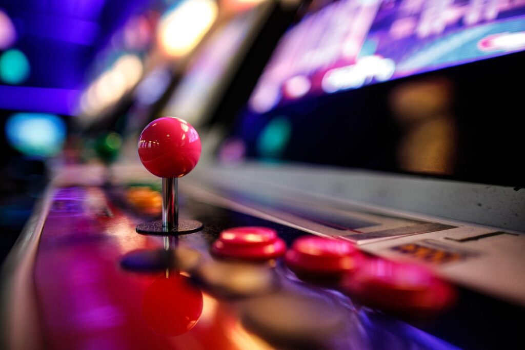 Red ball-top joystick and buttons on a retro arcade cabinet under neon light