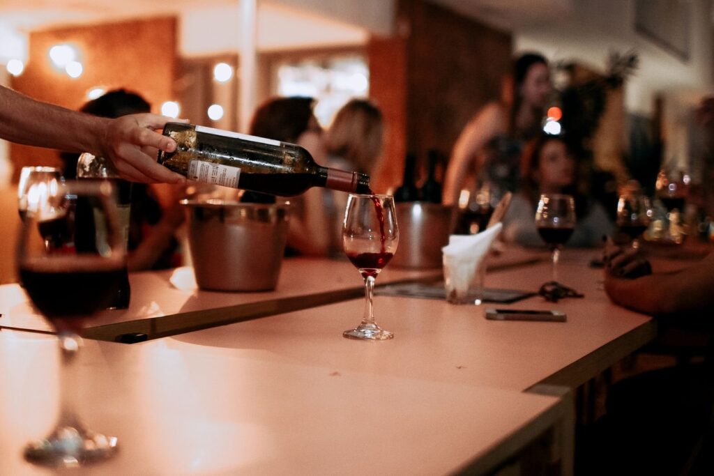 Server pouring red wine into glasses along a busy tasting bar