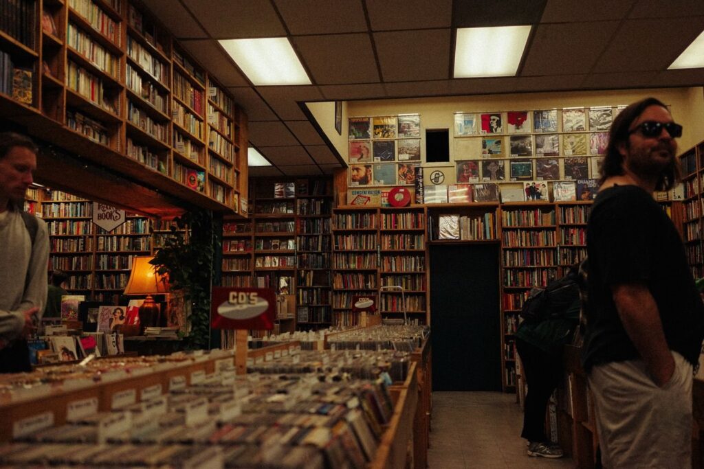 Shoppers browsing tall shelves of used books and bins of vinyl records in a dim independent store