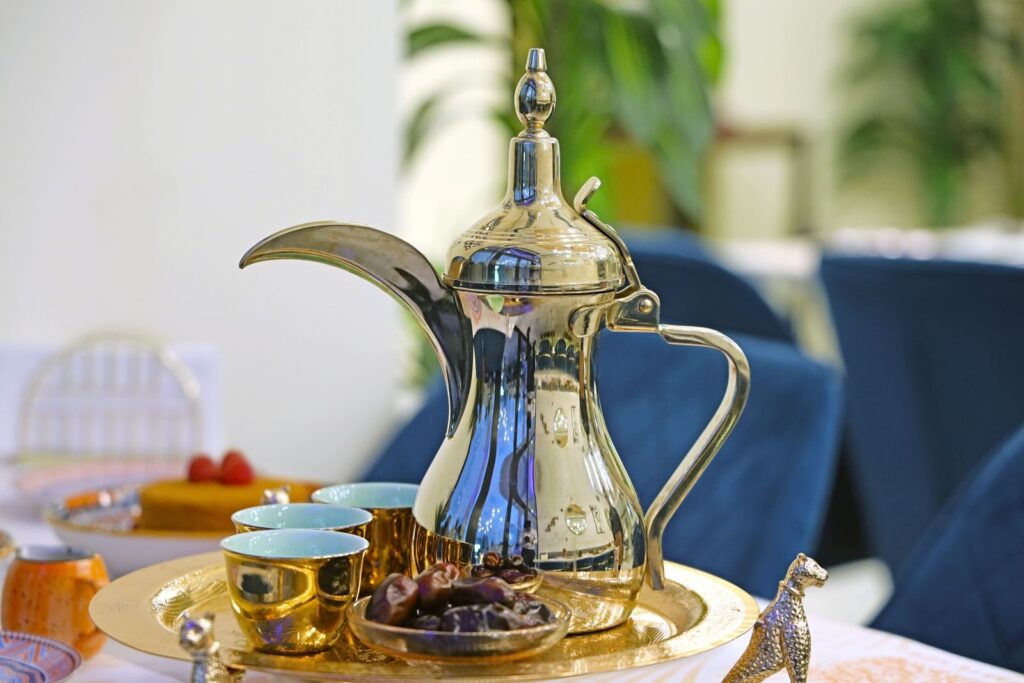 Silver dallah coffee pot on a tray with small gold cups and a dish of dates