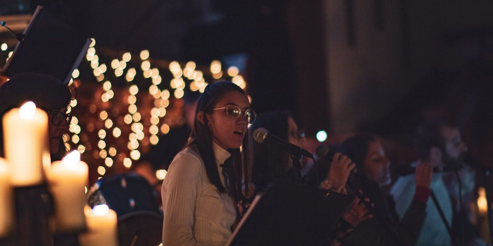 Singers performing by candlelight with string lights glowing behind them