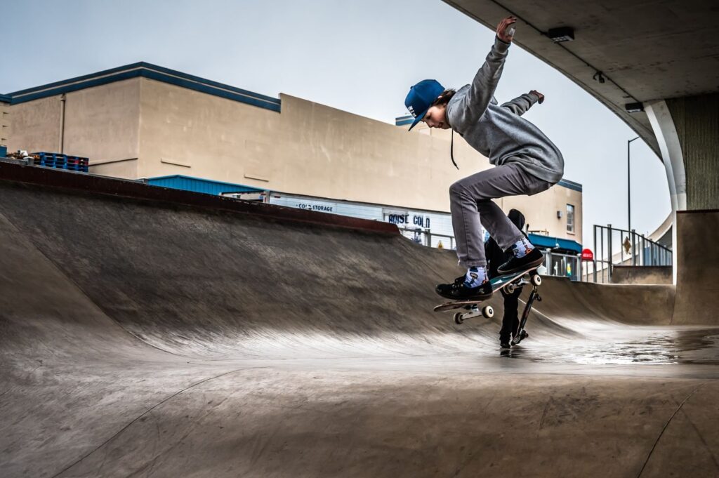 Skateboarder in a gray hoodie riding the lip of a concrete skate bowl