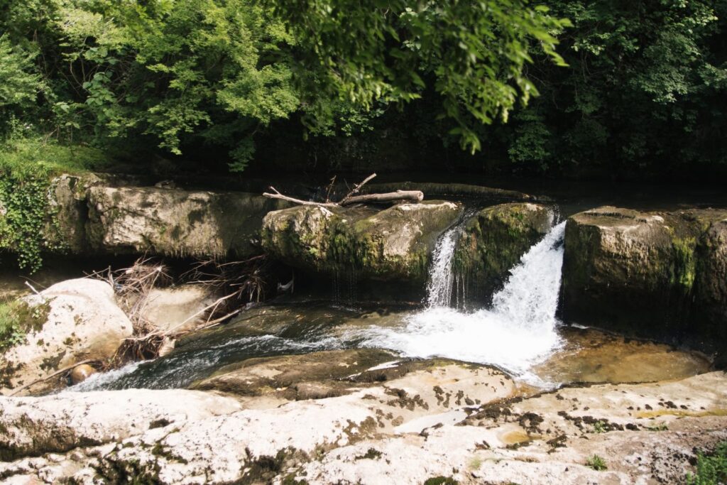 Small waterfall spilling over rocky limestone ledges into a shallow creek pool