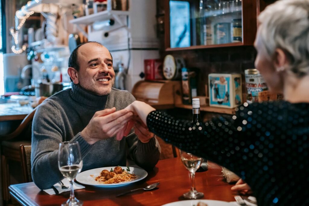 Smiling man holding hands with his date across a restaurant table set with pasta and wine